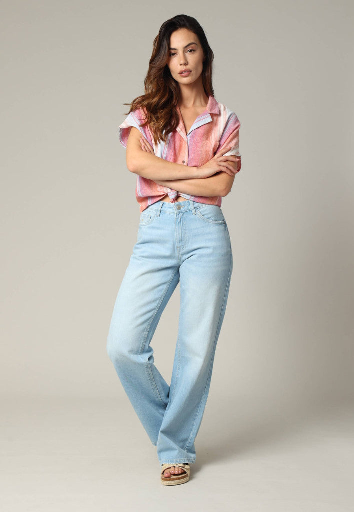 Woman wearing a striped shirt and light blue jeans against a plain background