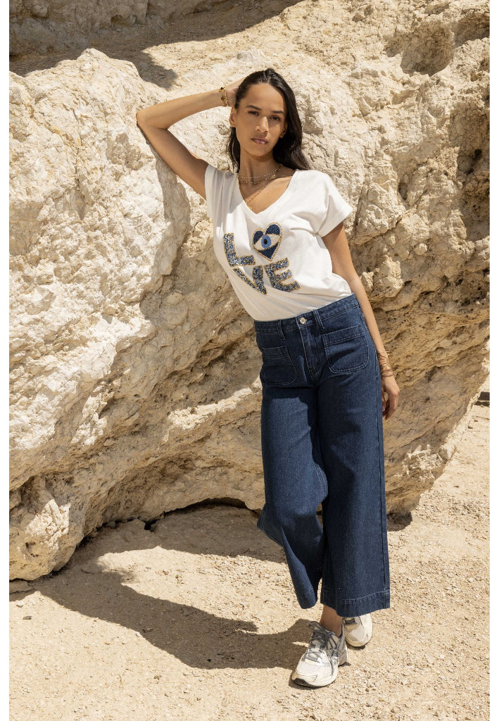 Woman wearing a white t-shirt with blue text and blue jeans standing against a rocky background