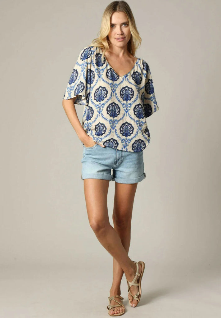 Woman wearing a patterned blouse and denim shorts on a plain background