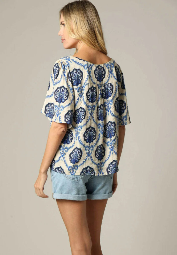 Woman wearing a blue and white patterned top with denim shorts on a neutral background