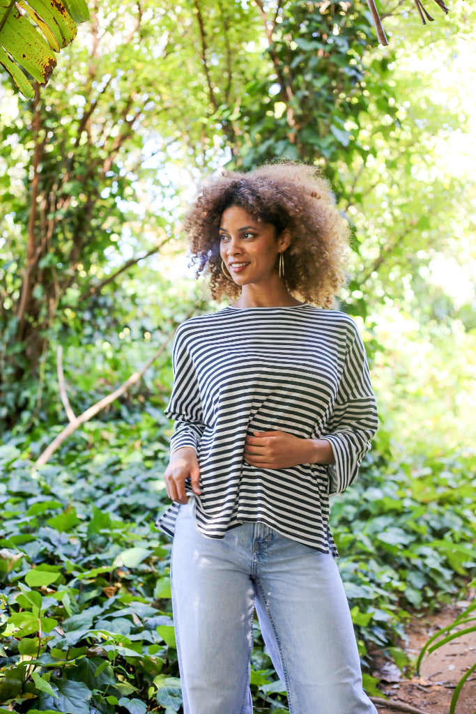 Woman wearing a striped shirt and jeans standing in a lush green forest.