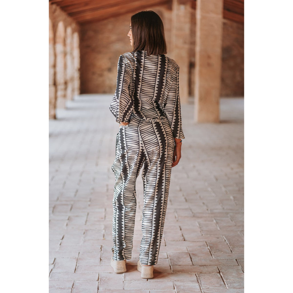 Woman in a patterned suit standing in a sunlit hallway with wooden beams.
