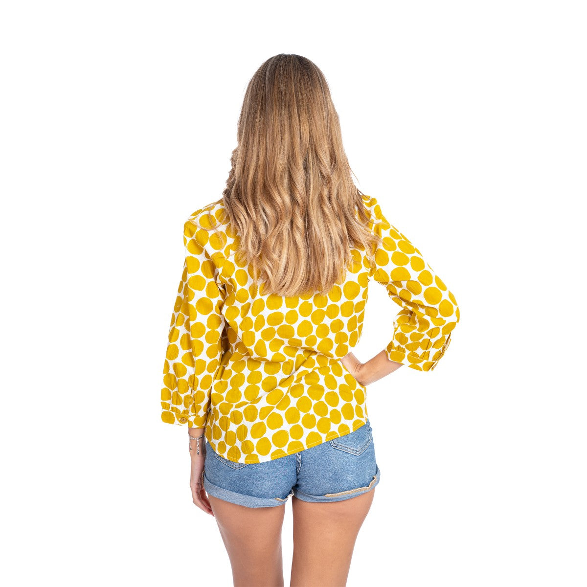 Woman wearing a yellow polka dot blouse and denim shorts on a white background