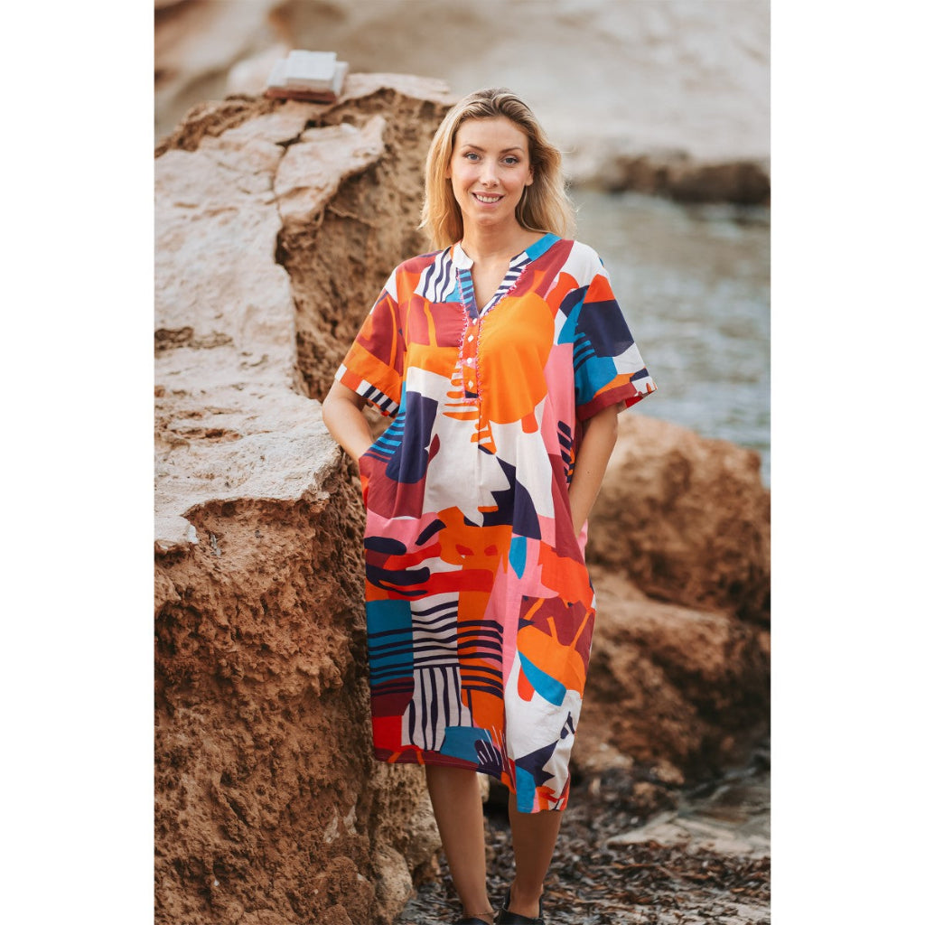 Woman wearing a colorful dress standing on a rocky beach.