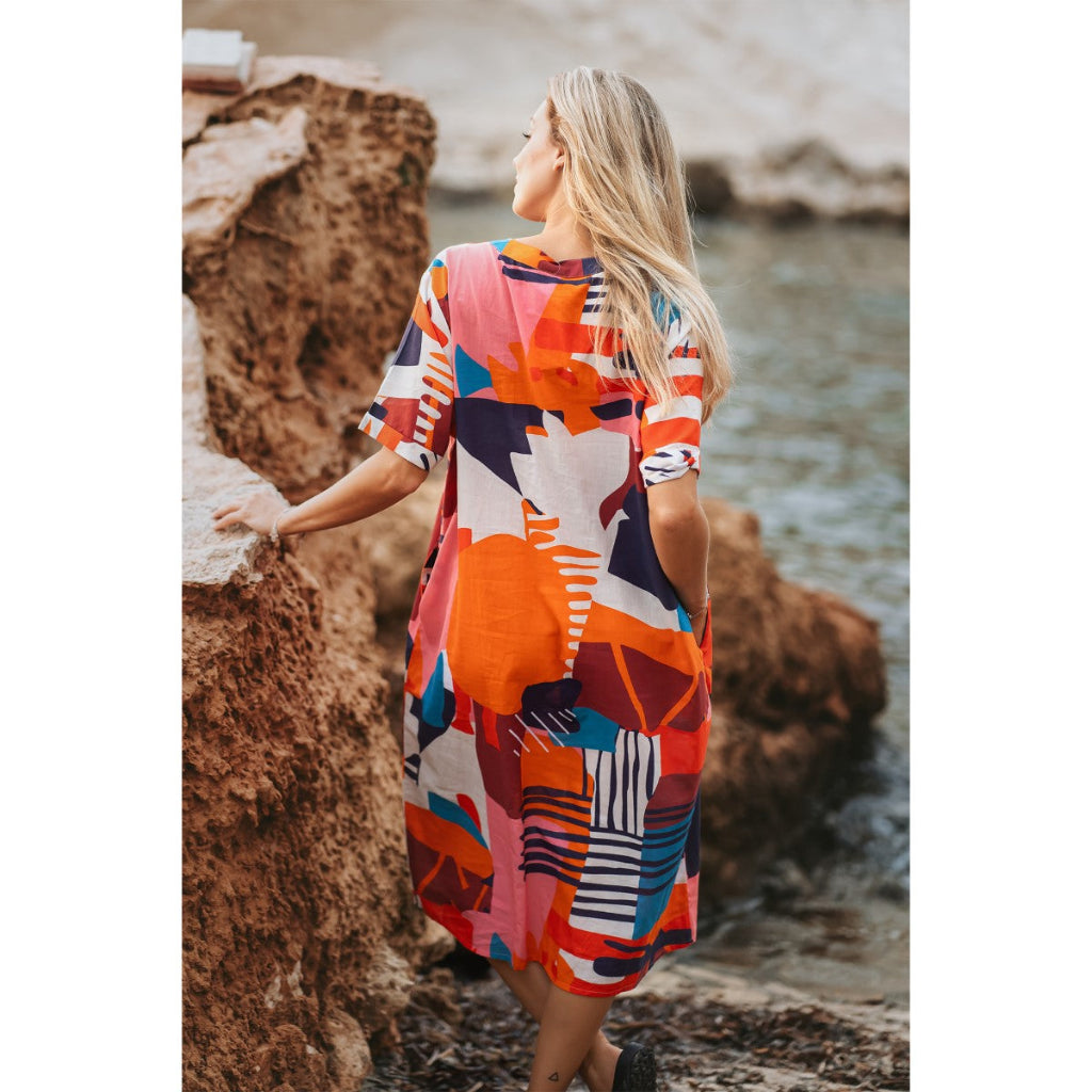 Woman in a colorful dress standing by a body of water.