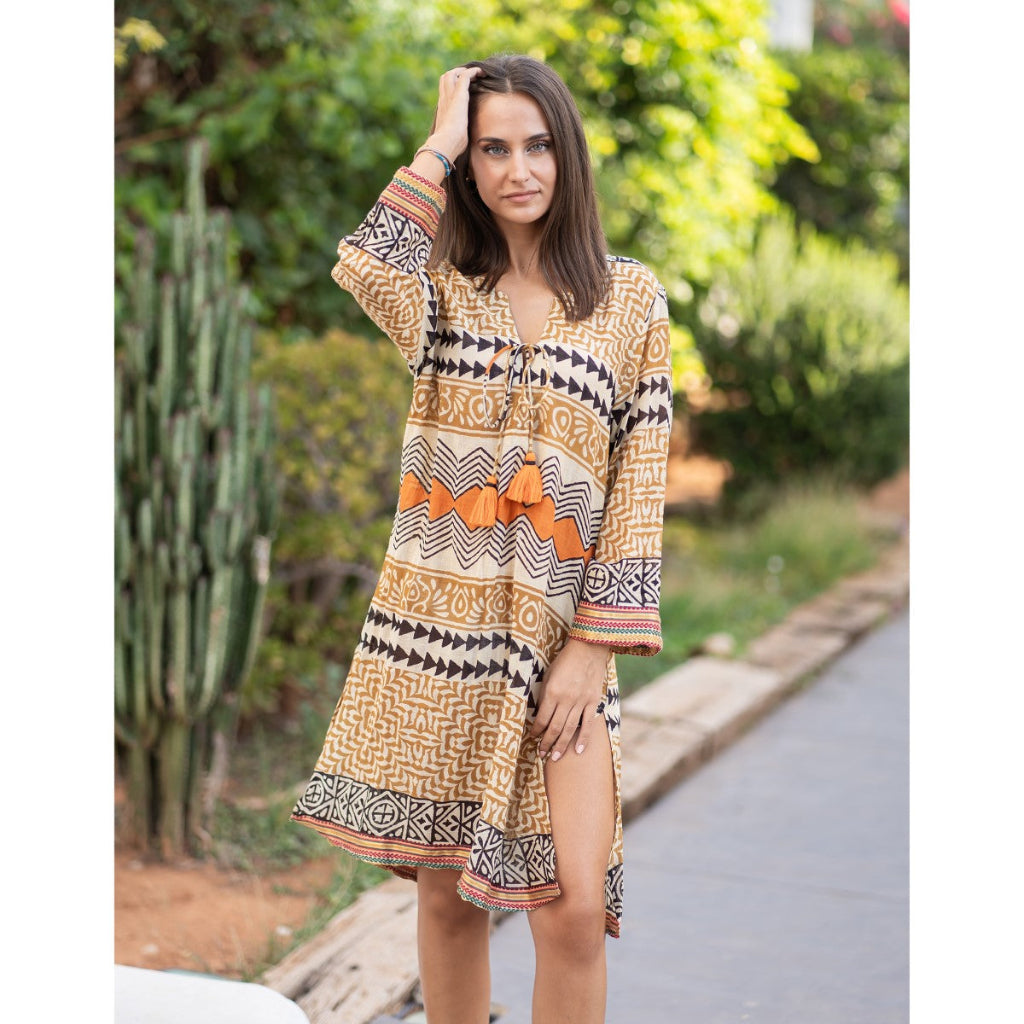 Woman wearing a patterned dress standing outdoors with greenery in the background