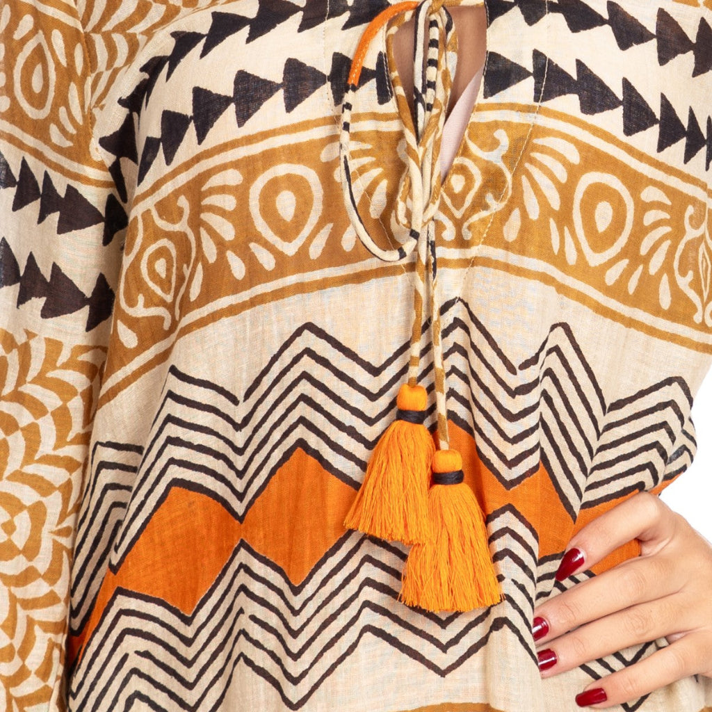 Close-up of a patterned fabric with tassels and a hand holding it.