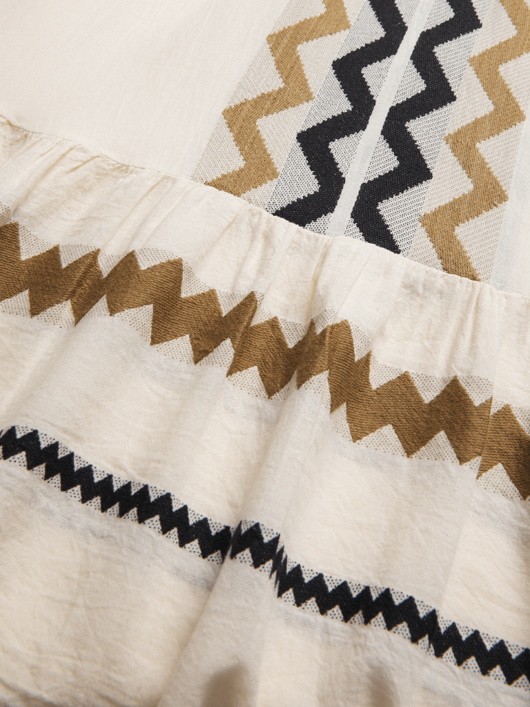 Close-up of a fabric with zigzag pattern in brown, black, and beige on a white background.