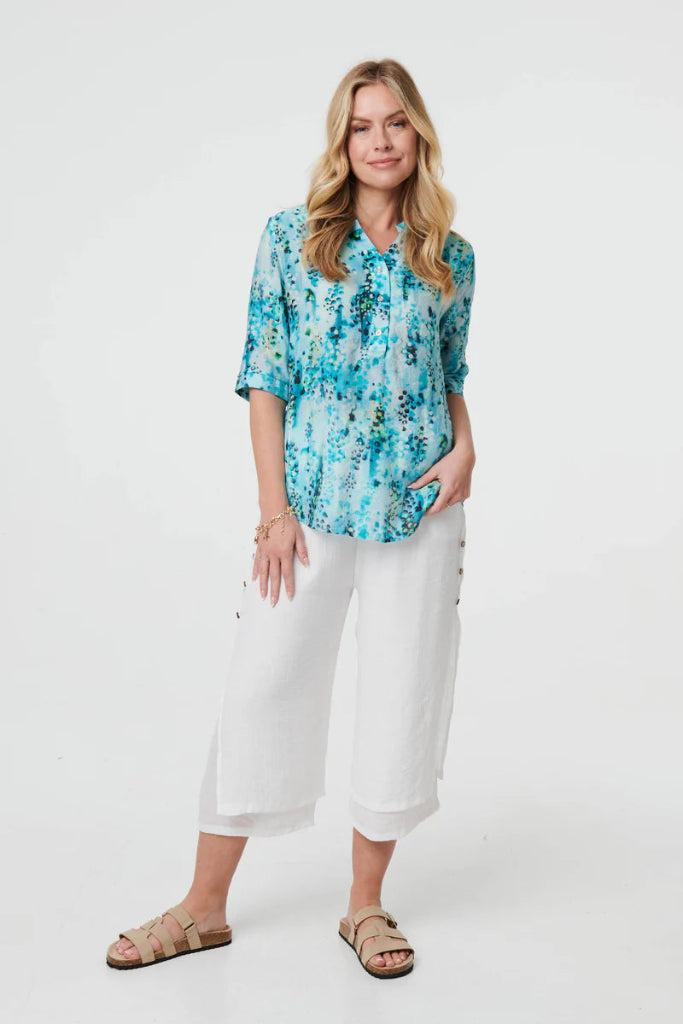 Woman wearing a blue floral blouse and white pants on a white background