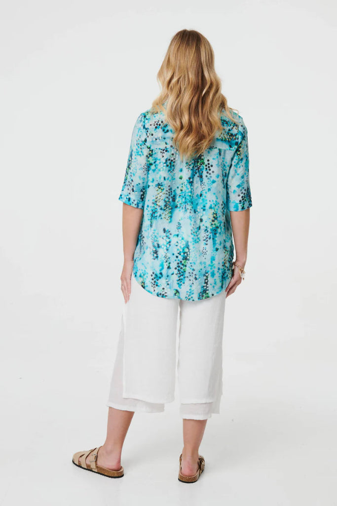 Woman wearing a blue floral blouse and white pants on a white background