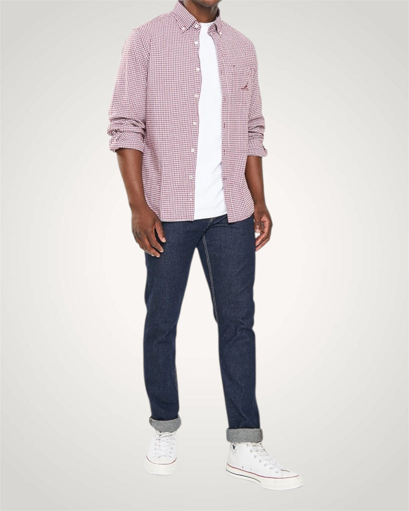 Person wearing a red checkered shirt, white undershirt, blue jeans, and white sneakers on a light gray background