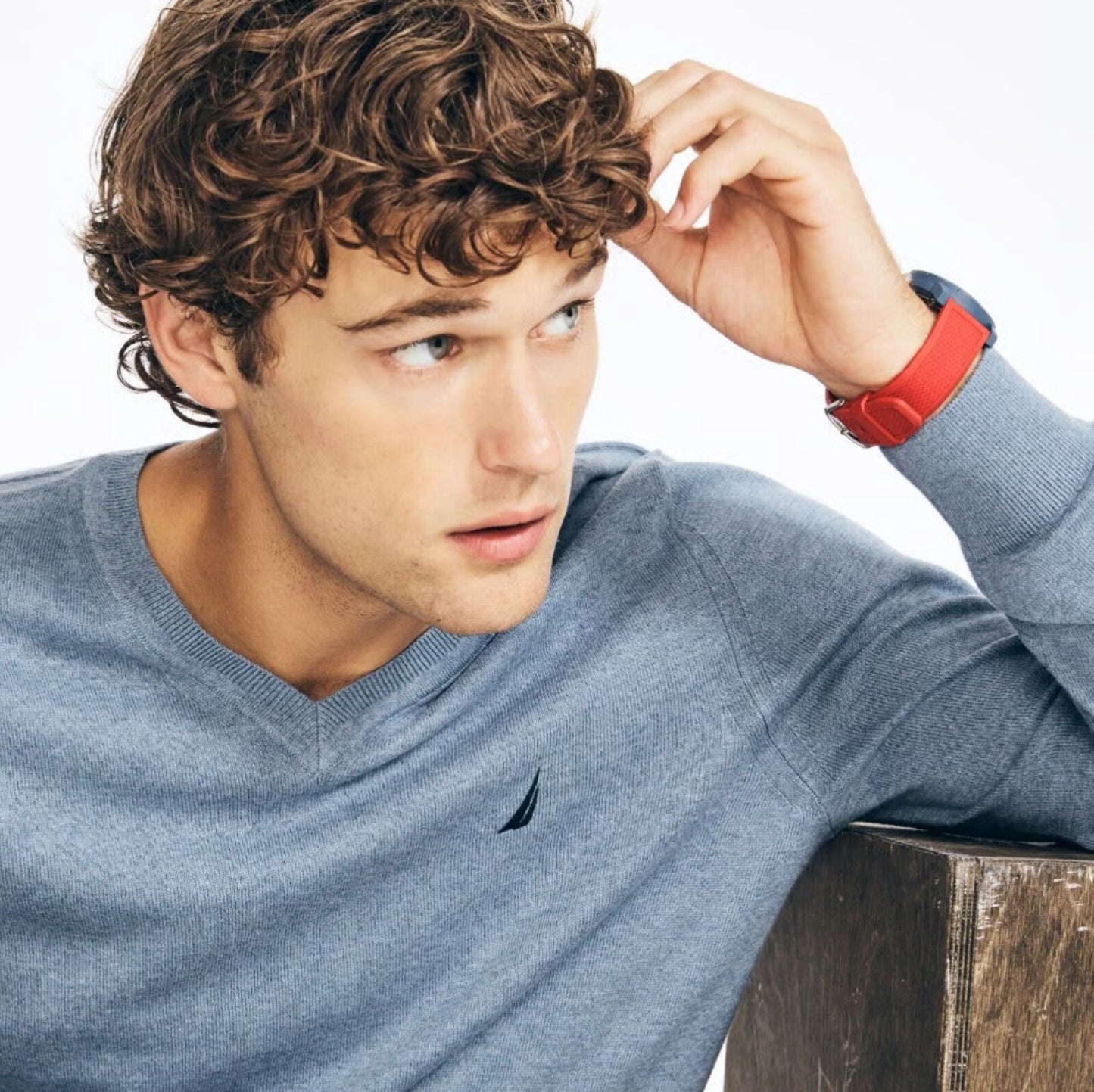 Man wearing a blue sweater with a red watch, sitting on a wooden surface.