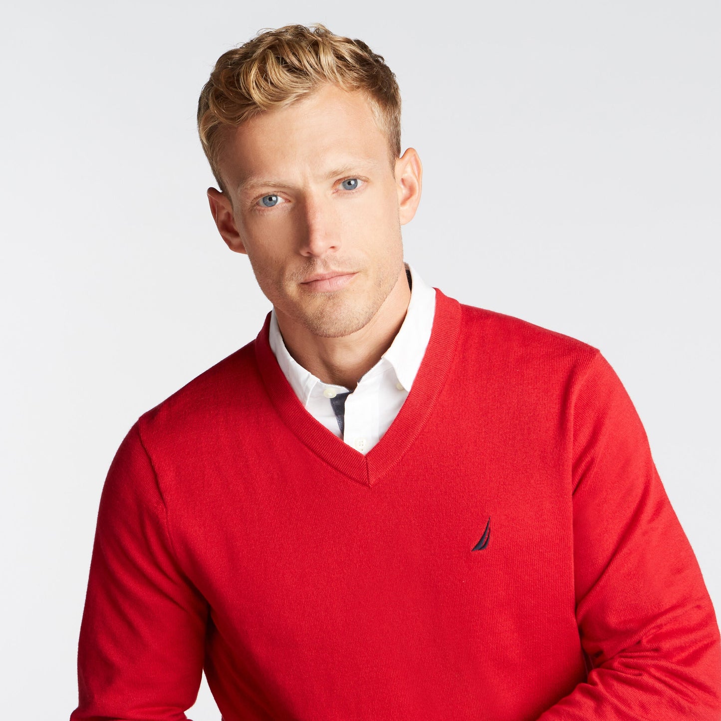 Man wearing a red sweater with a brand logo on a light gray background