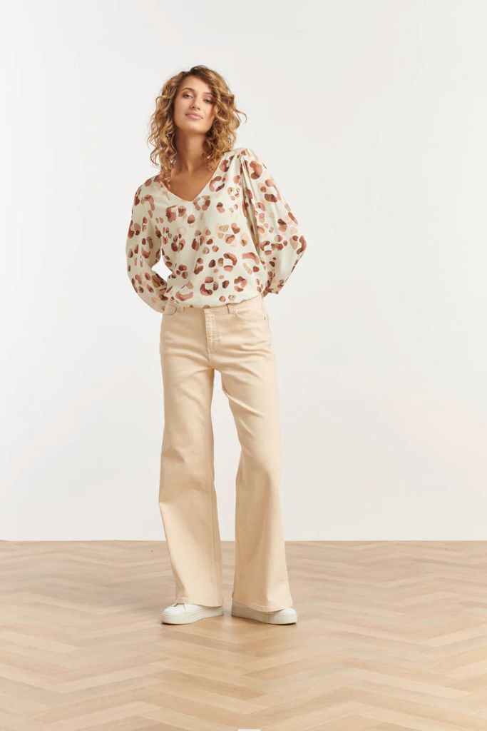 Woman wearing a Smashed Lemon animal print blouse and beige pants on a white background