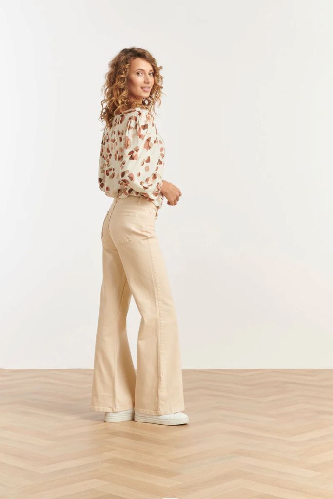 Woman wearing a floral blouse and beige flared pants on a white background