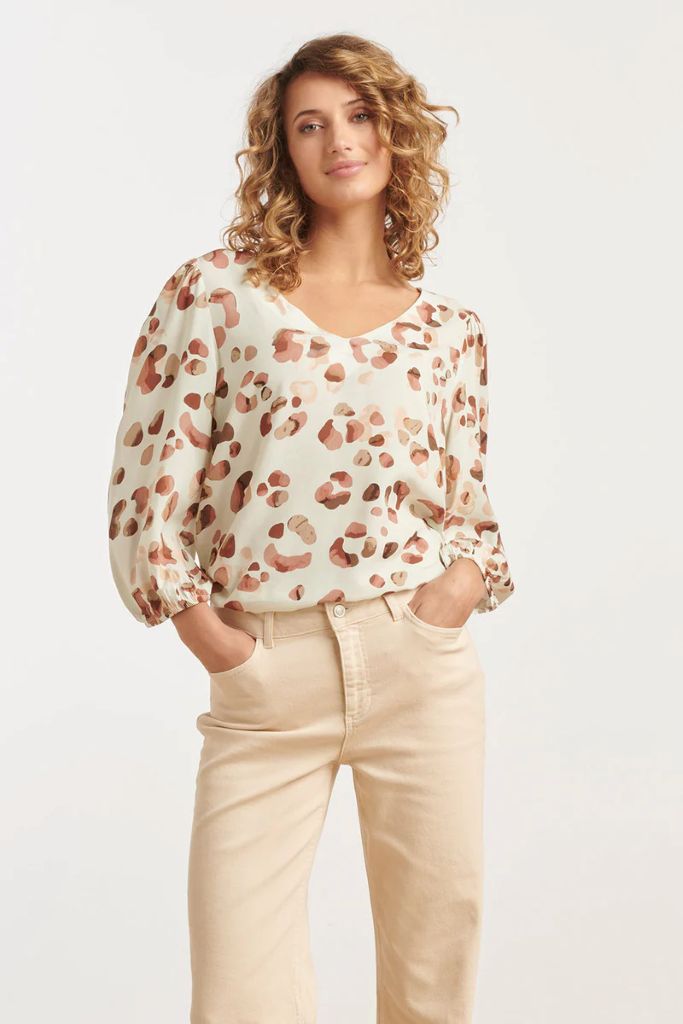 Woman wearing a Smashed Lemon patterned blouse and beige pants on a white background