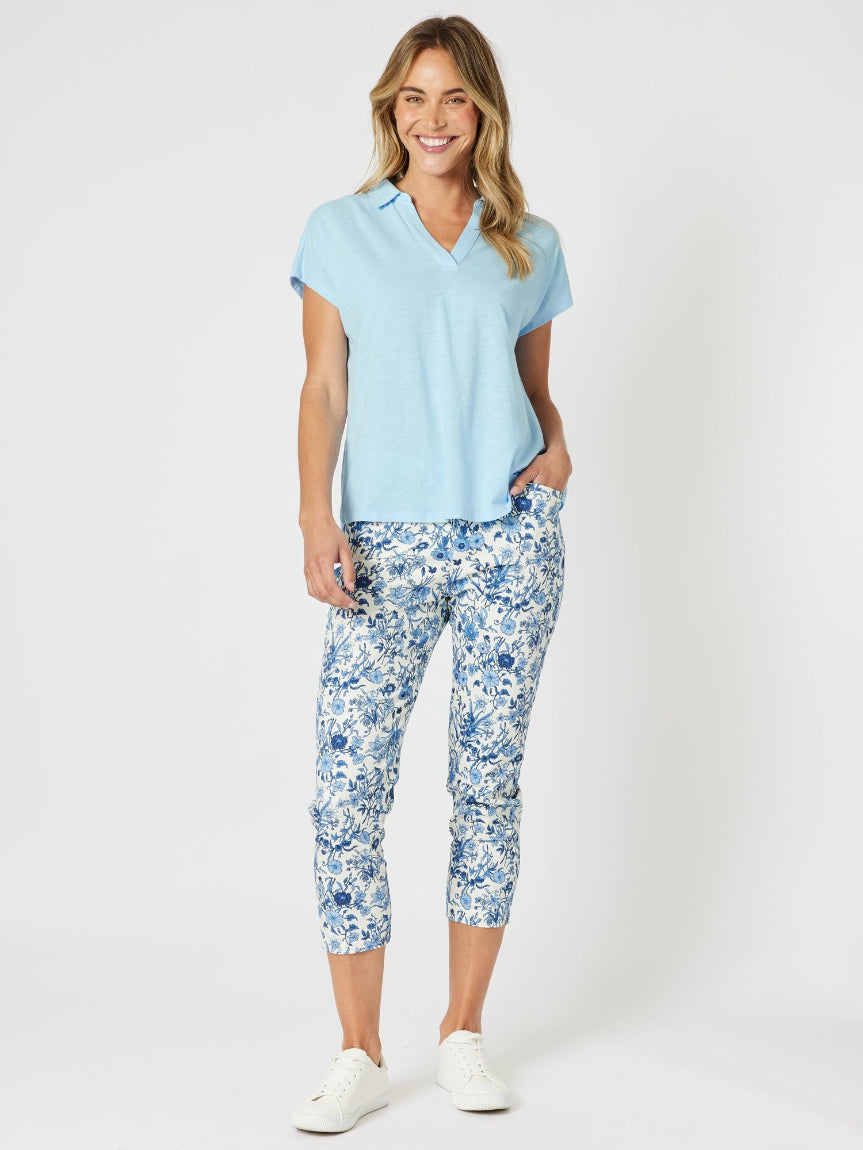 Woman wearing a light blue polo shirt and floral pants on a white background