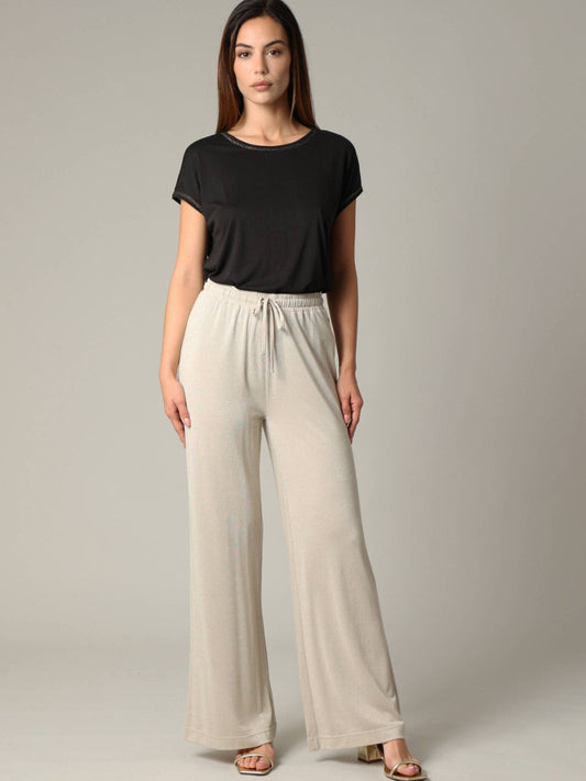 Woman wearing a black top and beige wide-leg pants on a plain background