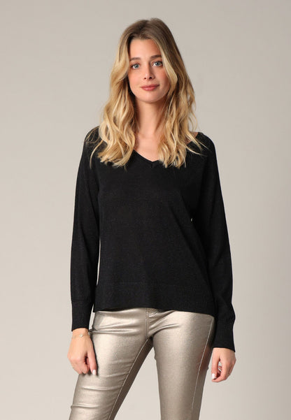 Woman wearing a black sweater and silver pants on a plain background