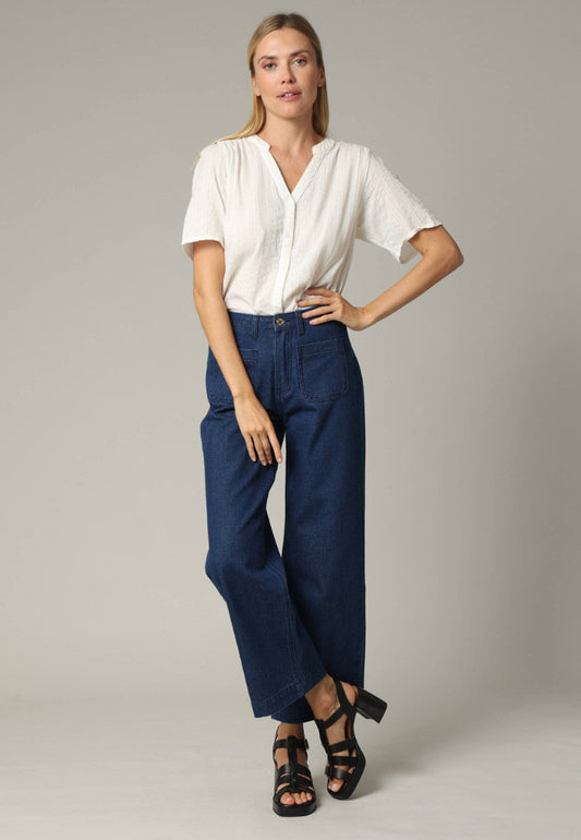 Woman wearing a white blouse and blue pants on a plain background
