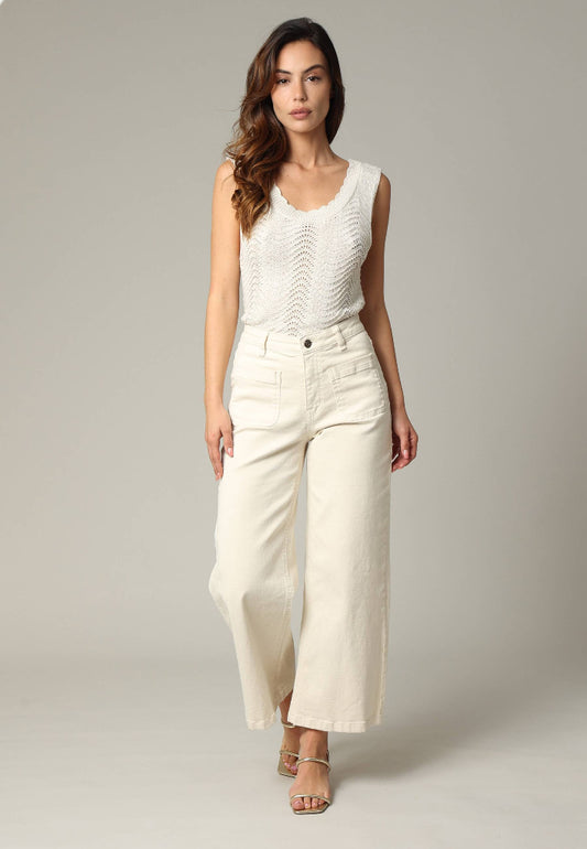 Woman wearing a white sleeveless top and cream-colored pants against a plain background