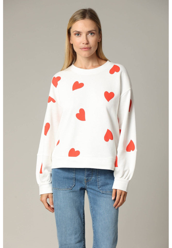 Woman wearing a white sweater with red heart patterns and blue jeans on a gray background