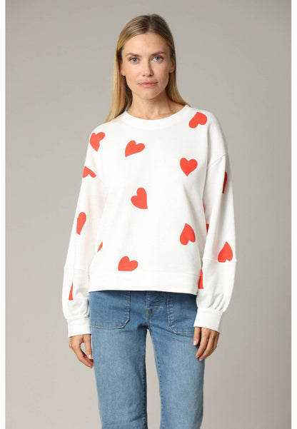 Woman wearing a white sweater with red heart patterns and blue jeans on a gray background