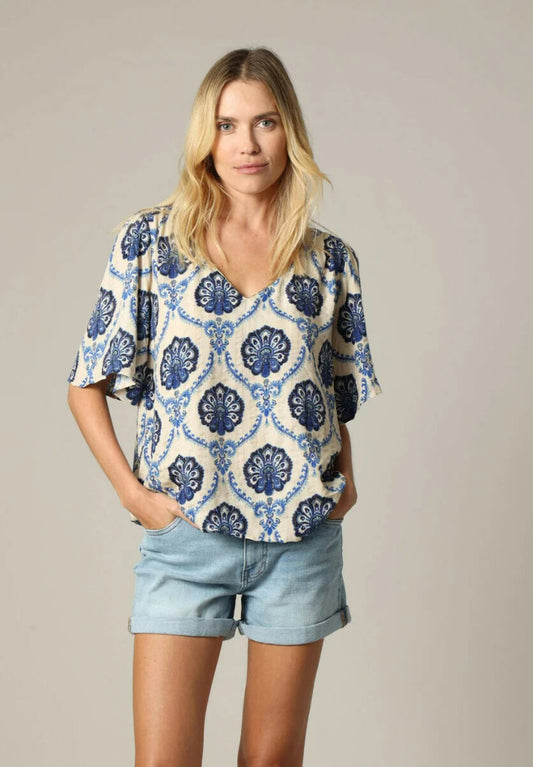 Woman wearing a blue and white patterned blouse with denim shorts on a neutral background