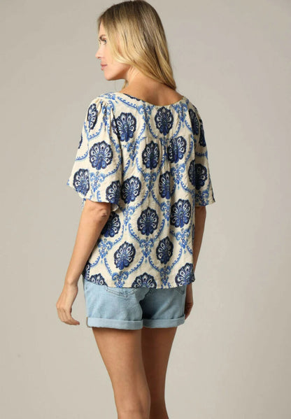 Woman wearing a blue and white patterned top with denim shorts on a neutral background