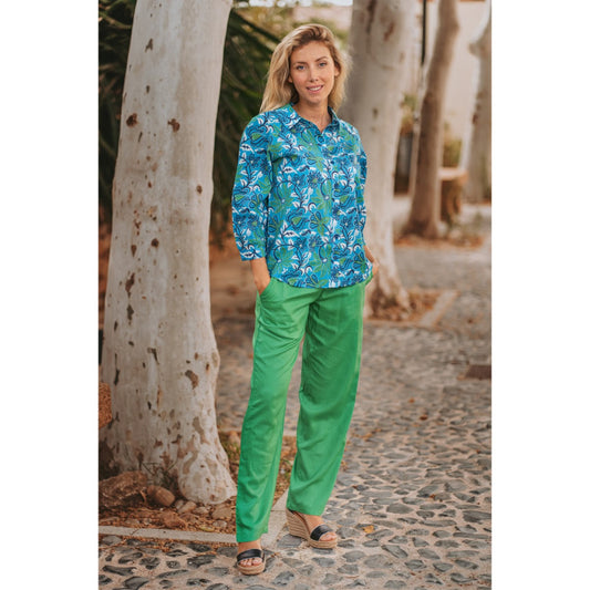 Woman wearing a blue floral shirt and green pants standing on a stone path with trees in the background.
