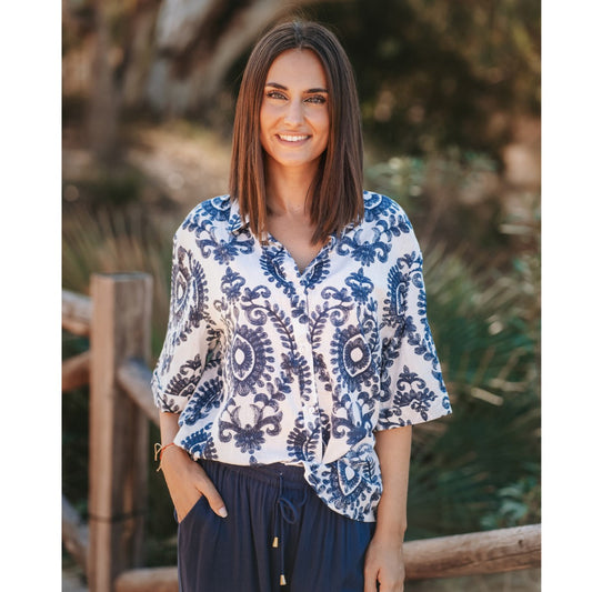 Woman wearing a blue and white patterned blouse with a blurred natural background