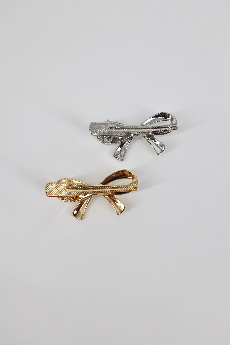 Two bow-shaped tie clips, one gold and one silver, on a light gray background.