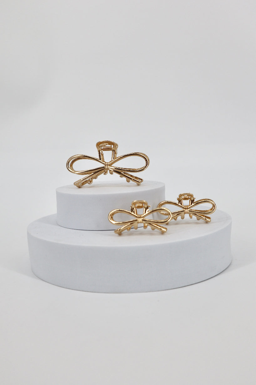 Gold hair clips on a white cylindrical stand against a white background