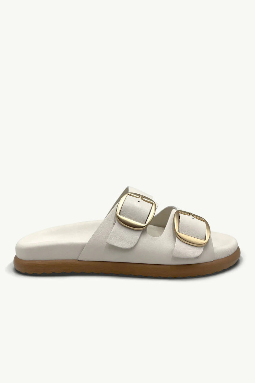 Neutral leather sandal with gold buckles against a studio background