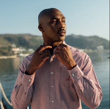 red gingham button down shirt Man adjusting his tie with a scenic background of water and hills.