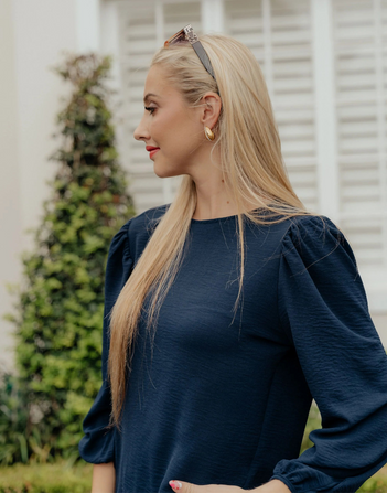 Woman wearing a navy blue top with puffed sleeves outdoors.