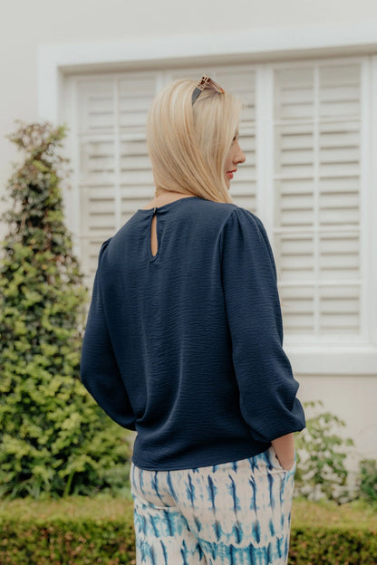 Woman wearing a navy blue top and patterned pants standing outdoors.
