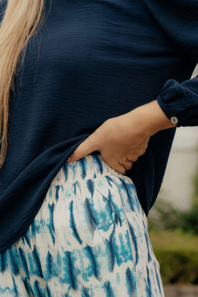 Person wearing a navy sweater and patterned skirt with blurred background