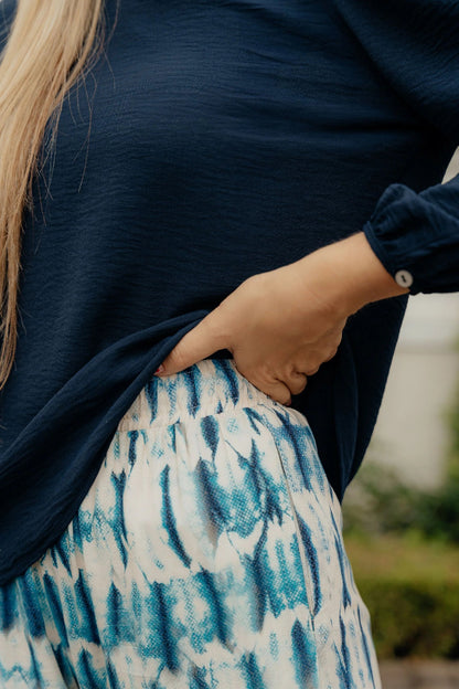 Person wearing a navy sweater and patterned skirt with blurred background
