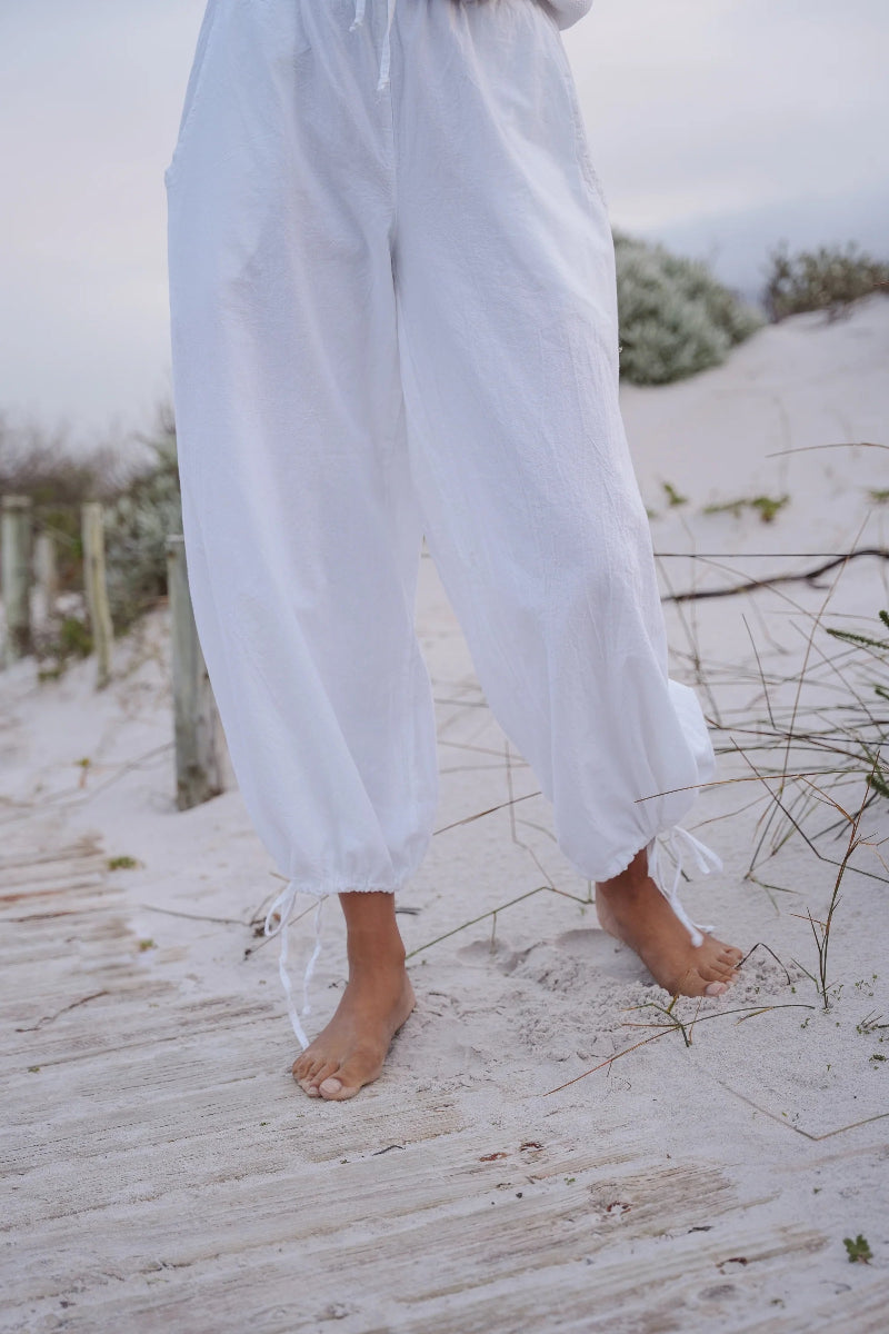 Person wearing white pants standing on a sandy beach with grasses in the background